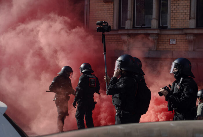 Aufnahme von Cops in voller Montur vor einer roten Pyrotechnik-Wolke.