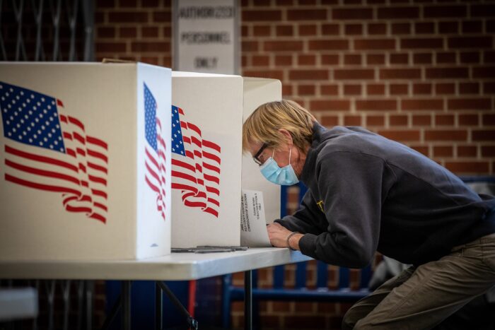 Ein Frau beugt mit Corona-Maske in einer Wahlkabine über ihren Wahlzettel.
