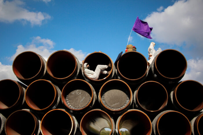 Personen in Maleranzügen mit Flagge auf Pipelineröhren.