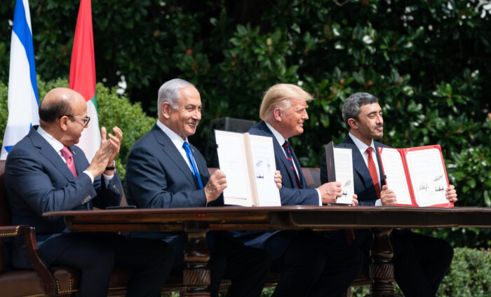 vier Männer im Anzug sitzen in einer am Tisch und halten unterzeichnete Verträge vor ihren Oberkörpern.