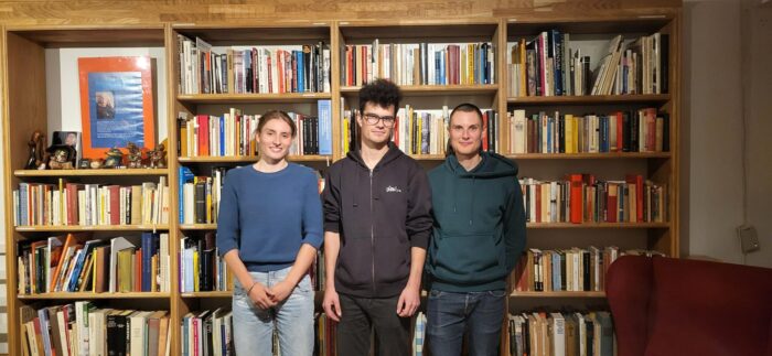 Bild von drei jungen Leuten vor einem Regal voller Bücher.