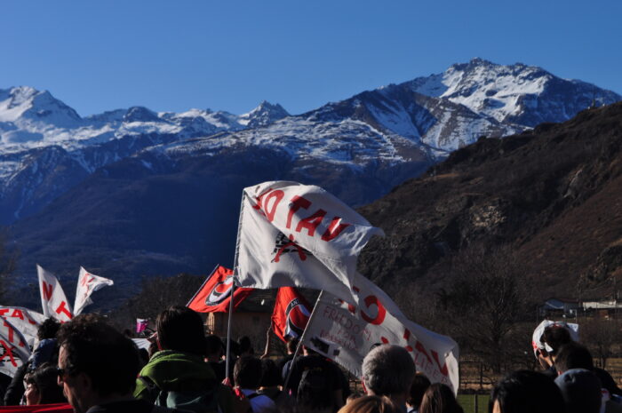 Ein Gruppe von Demonstrierenden mit Fahnen, im Hintergrund eine Berglandschaft
