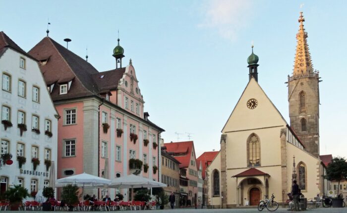 Ein mittelalterlicher Marktpplatz mit einer Kurche und einigen alten Häusern und einem Café