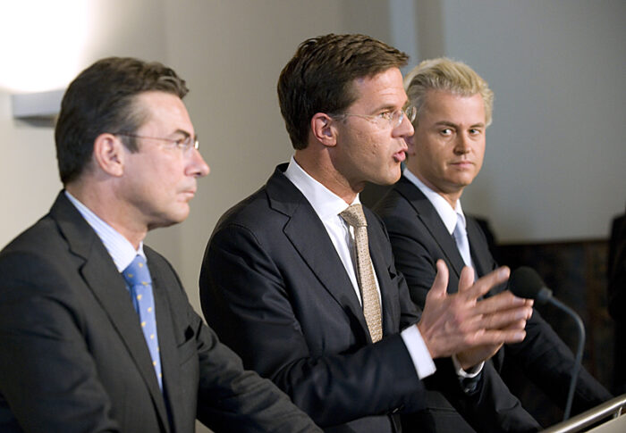 Drei Männer stehen an Rednerpulten. Der Mann in der Mitte redet, der rechts schaut ihm zu.
