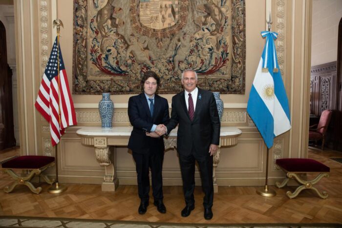 Javier Milei und der US-Botschafter Marc Stanley geben sich die Hand. Hinter ihnen die Flaggen der USA und Argentiniens.