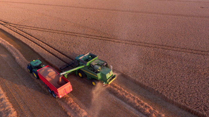 Ein Mähdrescher, neben ihm ein Traktor mit Anhänger auf einem Feld.