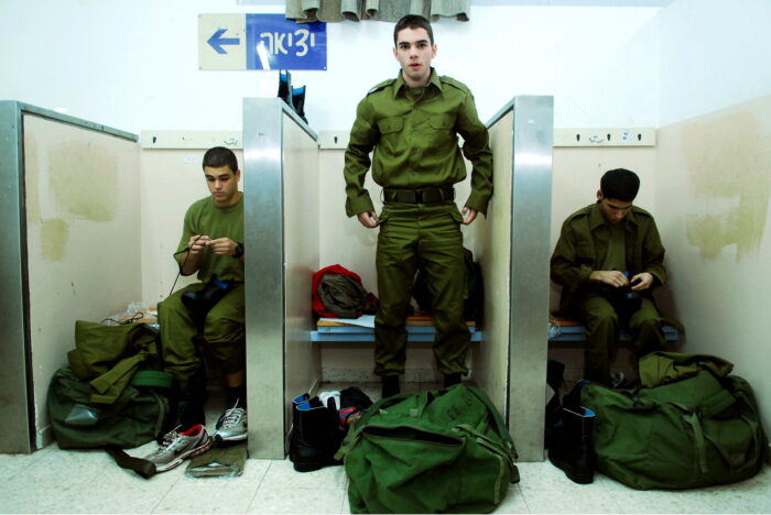 Bild einer Umkleidekabine. Drei israelische Soldaten passen ihre neue Uniformen an. Der Soldat in der Mitte steht und schaut in die Kamera.