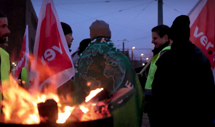 junge Leute mit ver.di- und Fridays-for-Future-Fahnen stehen im Morgengrauen um eine Feuertonne