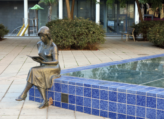 Eine lesende Person aus Bronze sitzt auf dem Rand eines Brunnens.