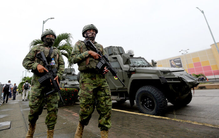 Zwei schwer bewaffnete Soldaten laufen durch die Straßen, hinter ihnen ist ein Militärjeep zu erkennen. Sie tragen ihre Waffen im Anschlag. Das Bild ist von schräg unten aufgenommen