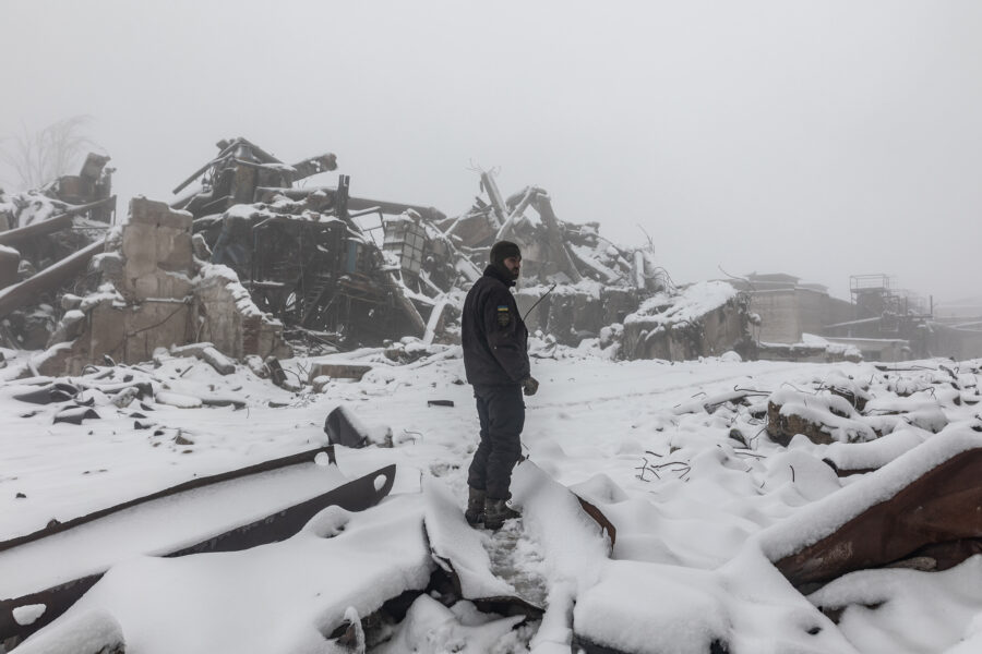 Ein Soldat steht mitten in einem verschneiten Trümmerfeld. Er schaut über die Schulter.