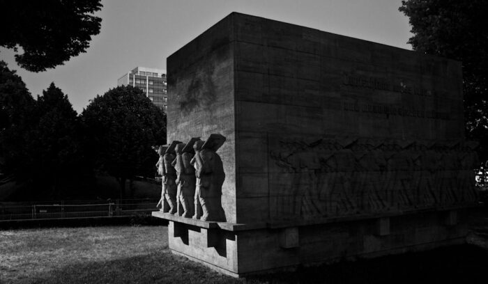 Eine klobiges Denkmal in der Nacht, an den Außenwänden des Quaders Plastiken marschierenden Soldaten