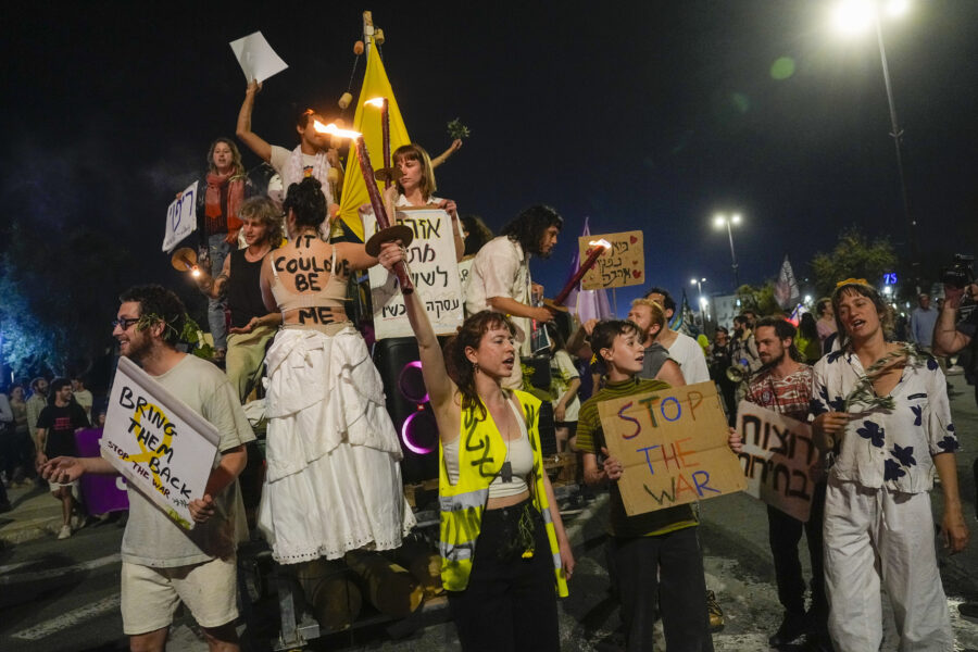 Auf dem Bild sieht man eine Gruppe von Menschen, teilweise verkleidet, die protestieren und Schilder hochhalten, auf denen Stop the War steht.