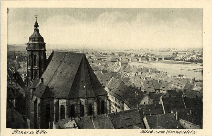 Alte Postkarte mit Schwarzweißfoto eines Blicks über eine Stadt. Im Vordergrund eine Kirche und mehrere Hausdächer, im Hintergrund ein Fluss mit Brücke. Am unteren Bildrand steht: Pirna a. Elbe. Blick vom Sonnenstein