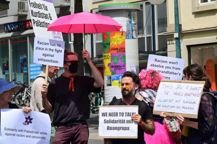 Eine Person mit einem rosa Schirm, weitere Personen mit Schildern