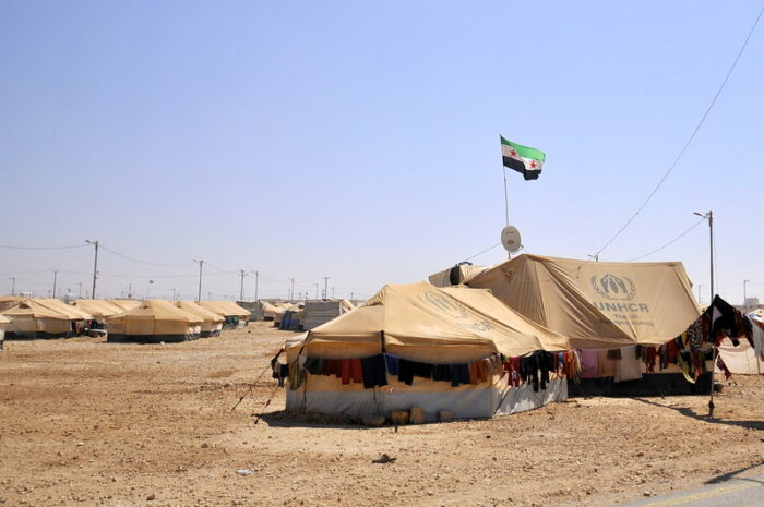 ein Zelt mit Fahne, dahinter weitere Zelte und sandiger Boden