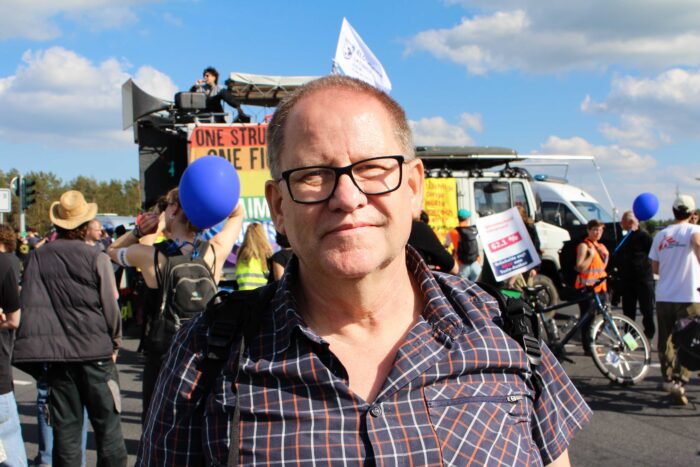 Ein älterer Mann in Karohemd und Brille steht in einer Demonstration
