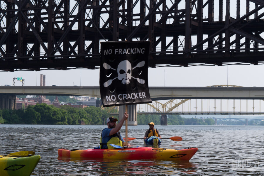 Zwei Leute in einem Kajak unter einer Brücke, die ein Schild mit Totenkopf und der Aufschrift "No Fracking - no Cracker" hochhalten.