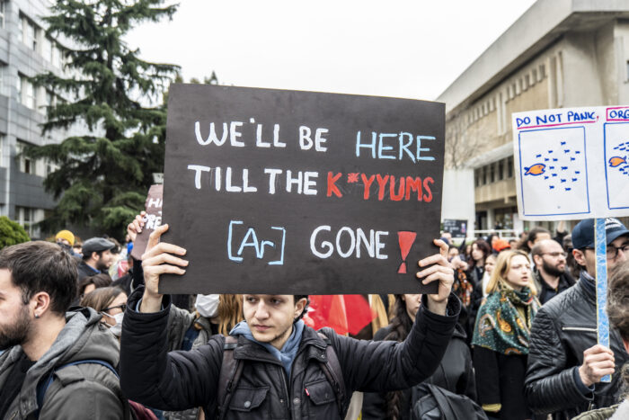 Ein Teilnehmer einer Demonstration in Istanbul hält ein schwarzes Plakat, auf dem in hellen Großbuchstaben "We'll be here till the k*yyums [ar] gone" steht. Hinter ihm stehen weitere Demonstrant*innen.