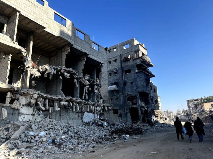 Drei Personen laufen an einem durch Israel zerstörten Gebäude in Gaza vorbei.