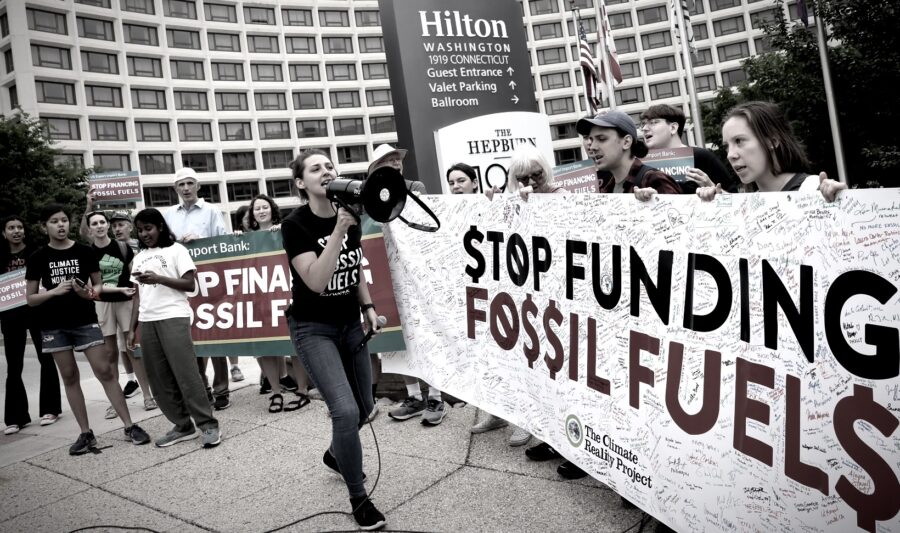 Eine Frau mit Megafon vor einem Transparent mit der Aufschrift "Stop Funding Fossil Fuels"