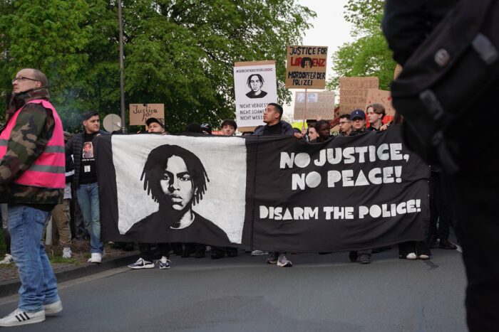 Zu sehen sind viele junge Menschen, die Schilder tragen und ein Transparent, auf dem steht No justice, no peace - disarm the Police, dazu ein Bild des getöteten Lorenz A.