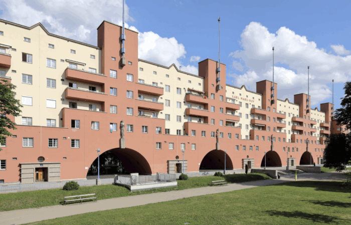 Karl-Marx-Hof in Wien, ein orange-gelbes Gebäude vor einem Rasen unter einem halb bewölkten Himmel