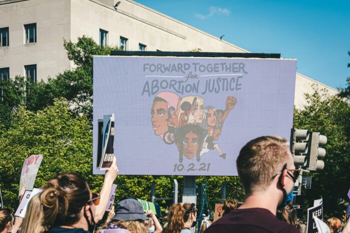 Man sieht demonstrierende Menschen, die ein Schild hochhalten auf dem steht Forward Together for Abortion Justice.