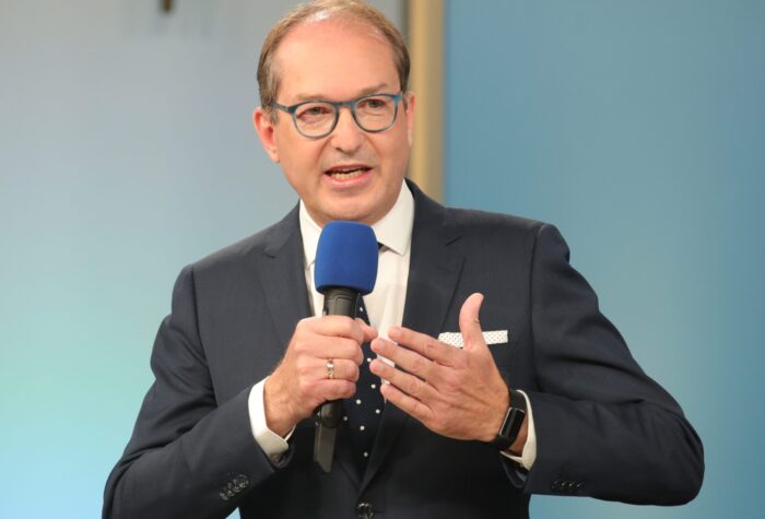 Das Bild zeigt Innenminister Alexander Dobrindt. Es ist von vorne aufgenommen. Dobrindt hält ein Mikrophon in der Hand und spricht offensichtlich zu einem Publikum.