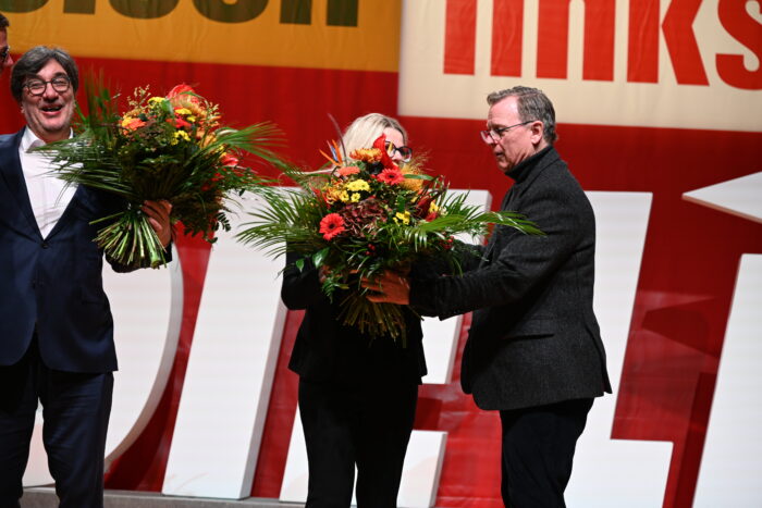 Man sieht eine Parteitagsbühne und Bodo Ramelow, der einer Person einen Blumenstrauß überreicht.
