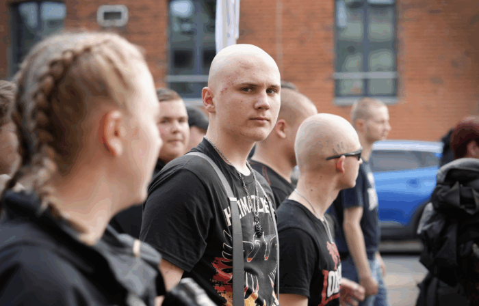 Junger Neonazi mit Glatze und Pickel schaut auf einer Demo in die Kamera
