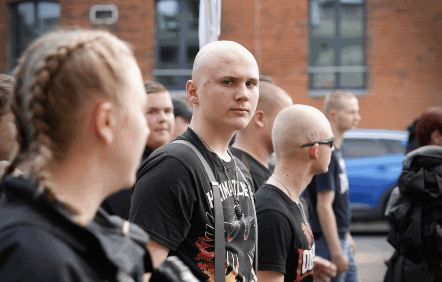 Junger Neonazi mit Glatze und Pickel schaut auf einer Demo in die Kamera