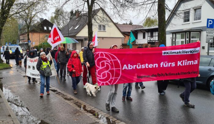 Ein rotes Demo-Transparent mit der Aufschrift "Abrüsten fürs Klima" an der Spitze eines kleinen Demo-Zuges. Zusätzlich ist eine ver.di-Fahne zu sehen.