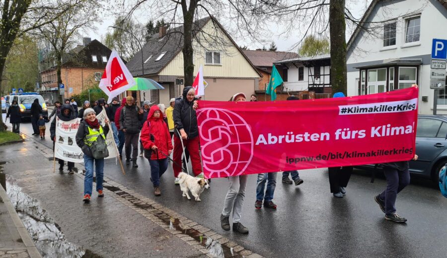 Ein rotes Demo-Transparent mit der Aufschrift "Abrüsten fürs Klima" an der Spitze eines kleinen Demo-Zuges. Zusätzlich ist eine ver.di-Fahne zu sehen.