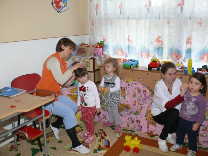 Man sieht eine Kindergartengruppe, mehrere Kinder und zwei Frauen, die sich um sie kümmern.