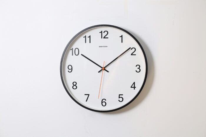 Eine Uhr an einer weißen Wand. Die Zeiger stehen auf 10:09.
