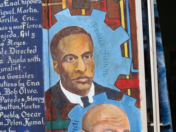 Ein Bild von Frantz Fanon an einer bunt bemalten Wand.