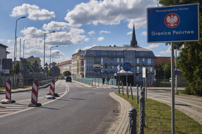 Zufahrt zu einer Brücke, im Vordergrund ist ein Schild mit der Aufschrift "Granica państwa" (Staatsgrenze) zu sehen.