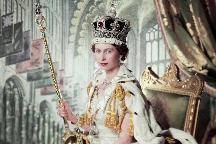 Die junge Queen Elizabeth mit Krone, Zepter und anderen königlichen Insignien auf einem Thron in einem bombastischen Raum