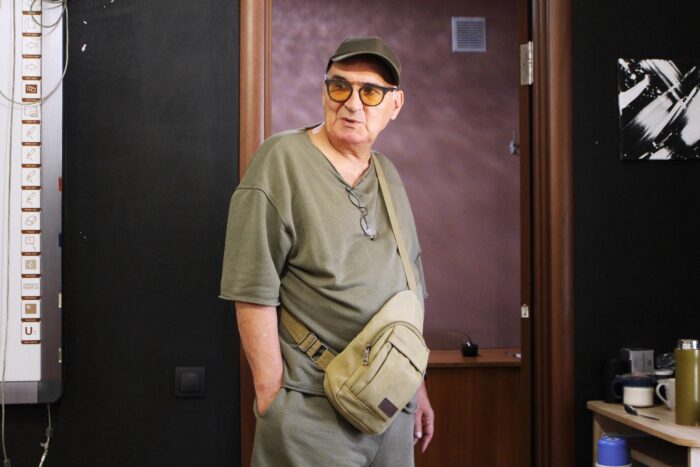 Ein älterer Mann mit armeegrünen kurzen Klamotten, Cap uind orange getönter Sonnenbrille
