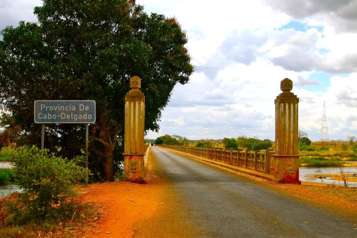 Aufnahme einer Brücke mit zwei Säulen aus der Kolonialzeit, links daneben ein Ortseingangsschild mit der Beschriftung "Provincia de Cabo Delgado"