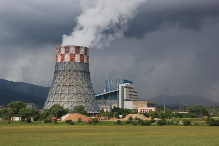 Im Vordergrund eine grüne Wiese, im Hintergrund der Kühlturm eines Kohlekraftwerks mit weißem Rauch.