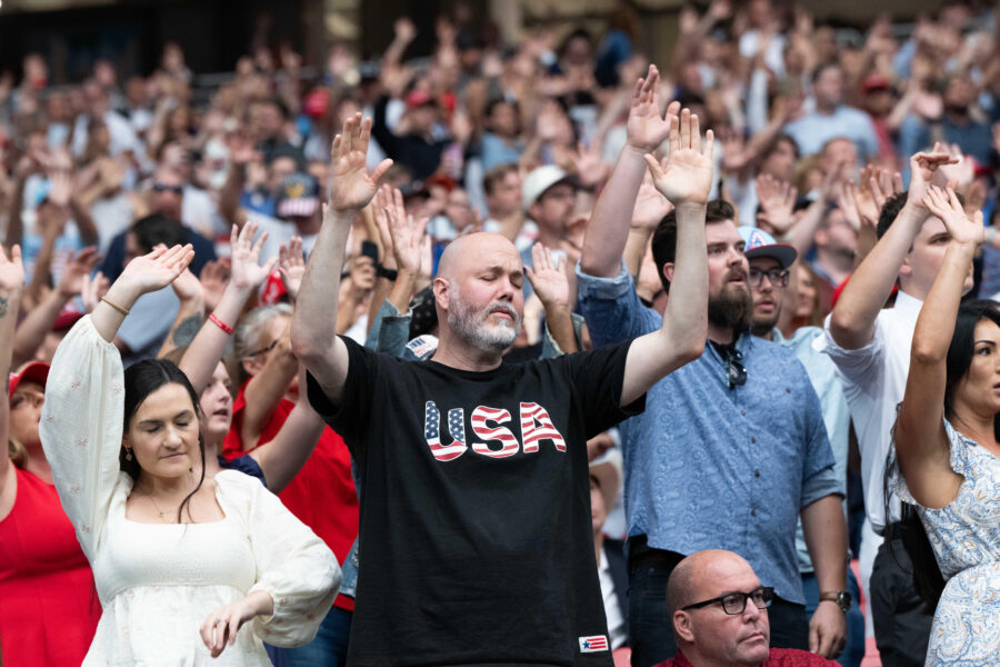 Man sieht eine Menschenmenge, die mit geschlossenen Augen und erhobenen Händen betet.
