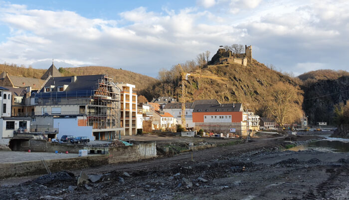 Im Hintergrund eine Burg auf einen Berg, davor ein paar Häuser und eine Schneise der Zerstörung.