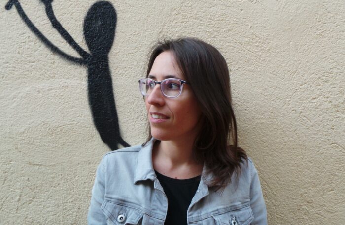 Man sieht die Autorin Eva Blatasar, schulterlange braune Haare, Brille, in Großaufnahme, zur Seite blickend.