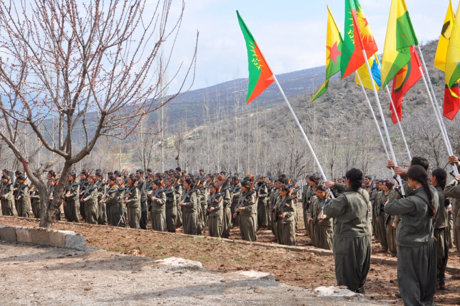 Die PKK-Guerrilla in den Bergen ist mit Waffen und Fahnen ihrer Organisationen in Reihen aufgestellt.