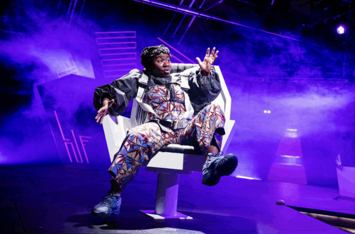 Eine Person sitzt in einem Drehstuhl und macht eine ausladende Bewegung. Hinter ihr blaues Licht