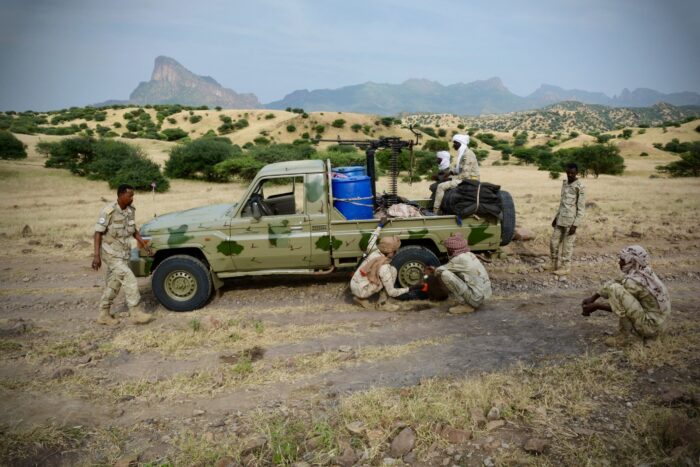 Militär-Pick-up mit Maschinengewehr auf einer Sandstraße, um das Auto stehen und hocken Männer in Uniformen