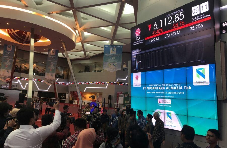 Ein großer Display, der Börsennotierungen anzeigt, davor Börsenhändler.