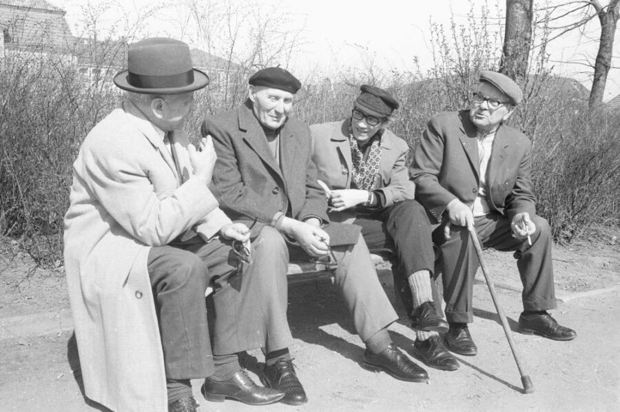 Vier ältere Herren sitzen auf einer Bank und unterhalten sich. Eine schwarz-weiß Aufnahme.